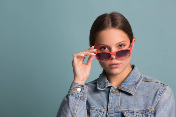 portrait of a beautiful young woman in sunglasses on a blue background - Photo, image