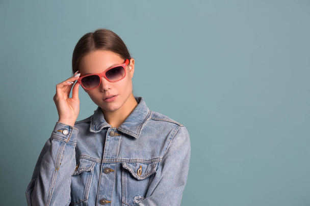 portrait of a beautiful young woman in sunglasses on a blue background - Valokuva, kuva