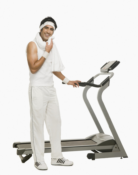 Man wiping his face with a towel beside a treadmill - Φωτογραφία, εικόνα