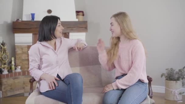 Portrait of Caucasian mother and adult daughter sitting on couch, talking and laughing. Positive teen girl having fun with mom at home. Relationship, family, happiness. - Video