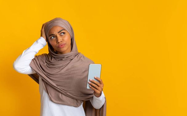 Thoughtful afro muslim girl holding smartphone and touching her head - Фото, изображение