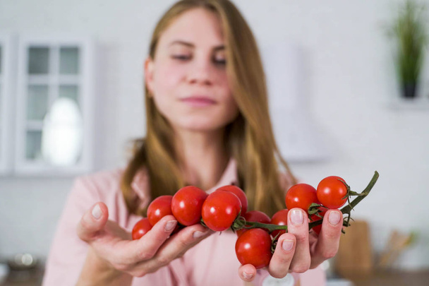 The girl holds in her hands a large branch of red cherry tomato. - Foto, Imagem