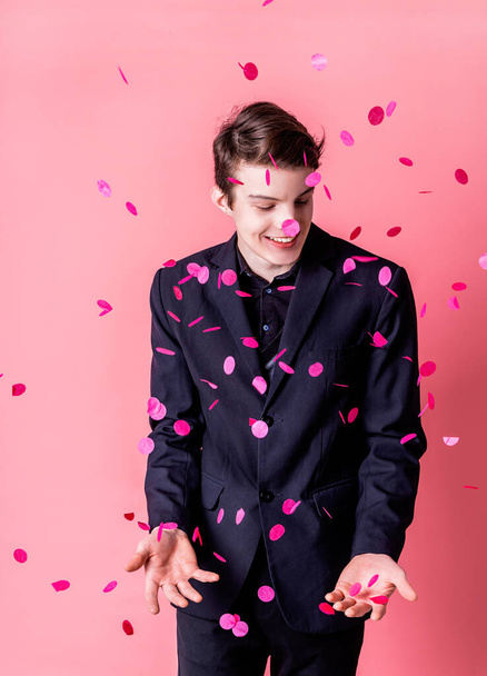 Счастливый молодой человек с розовыми летающими конфетти на вечеринке на розовом фоне
 - Фото, изображение