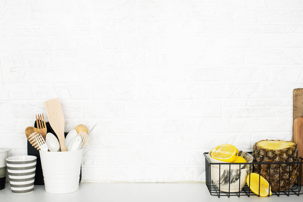 Kitchen shelf with baskets for storing products, pineapple, lemons, cutlery in a glass, chopping wooden boards on a white brick background. Style home scandi minimalism trend of modernity. Copy space - Foto, afbeelding