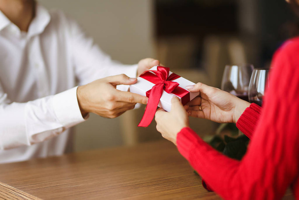 Man gives to his woman a gift box with red ribbon. Hands of man gives surprise gift box for girl. Young loving couple celebrating Valentine's Day.  Relationship, surprise, Birthday concept. - Фото, изображение
