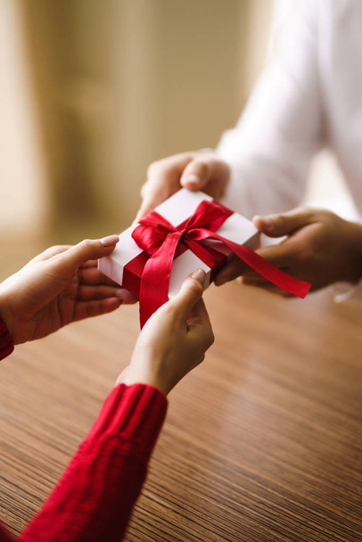 Man gives to his woman a gift box with red ribbon. Hands of man gives surprise gift box for girl. Young loving couple celebrating Valentine's Day.  Relationship, surprise, Birthday concept. - 写真・画像