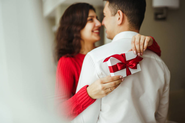 Happy couple with gift hugging. Cheerful couple with gift in hands enjoying each other. Valentines day celebration concept. Relationship, surprise and love concept. - Valokuva, kuva