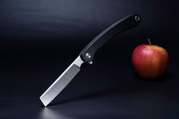 Cuchillo de afeitar y manzana. Navaja y manzana sobre fondo negro
. - Foto, imagen
