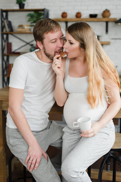 Schwangere und Ehemann frühstücken in der Küche Kaffee oder frischen Saft trinken und küssen. - Foto, Bild