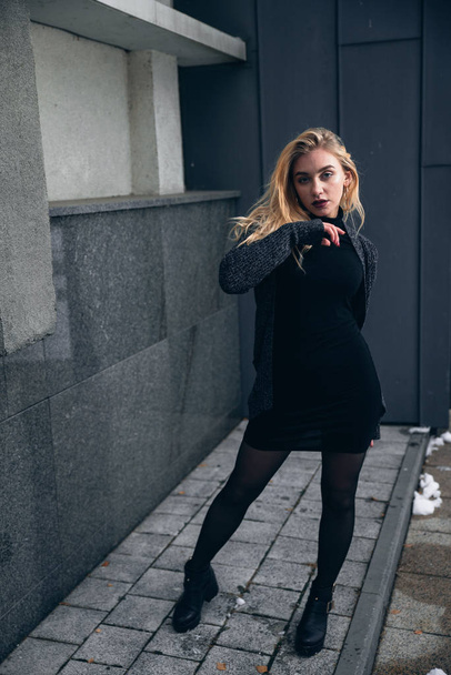 Girl in a black dress in the winter on a background of a dark building - Foto, afbeelding