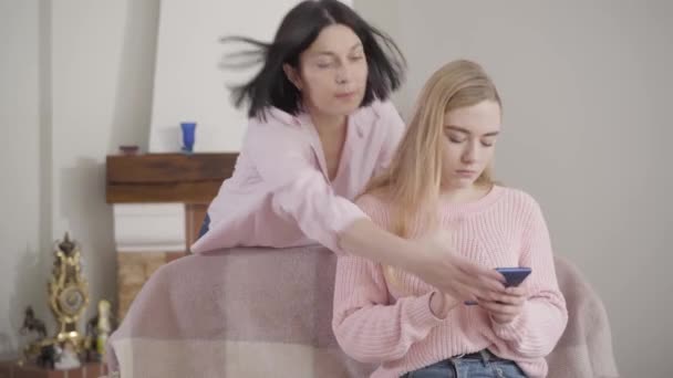 Adult brunette Caucasian woman taking away daughters smartphone. Mother scolding young teen girl at home. Misunderstanding, conflict, generations. - Filmagem, Vídeo