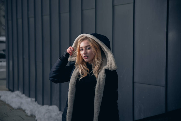 Girl in a black dress in the winter on a background of a dark building - Valokuva, kuva