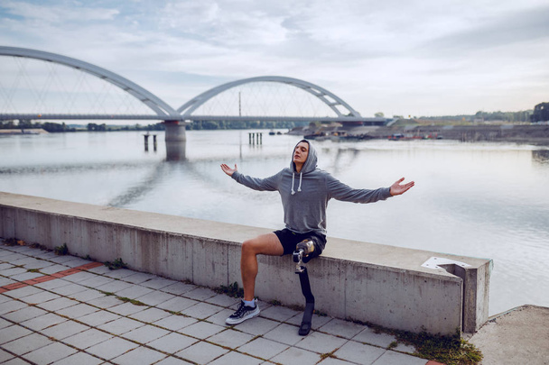 Вмістити здорового білоруського спортсмена з штучною ногою і светром на голові, сидячи на набережній з відкритими руками
. - Фото, зображення