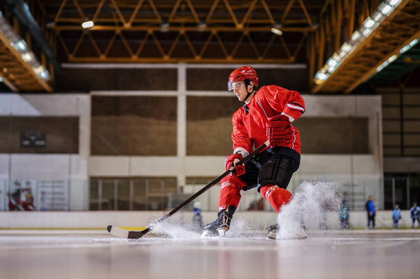 Volledige lengte van de Kaukasische hockeyspeler die ijshockey speelt in de hal. - Foto, afbeelding