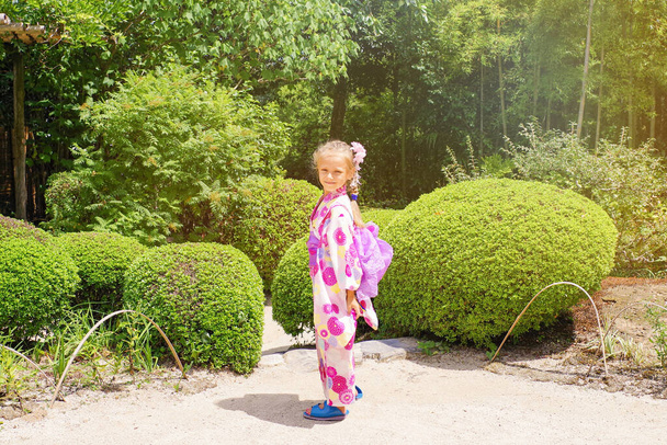 Japanilaiseen kimanoon pukeutunut eurooppalainen tyttö kävelee japanilaisessa puutarhassa. Japanilainen puutarha, japanilainen kulttuuri
. - Valokuva, kuva
