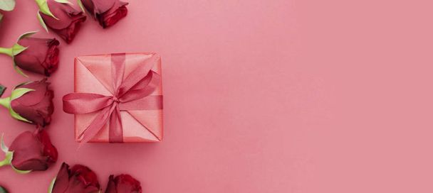 Baner Walentynki, czerwone róże i pudełko z wstążką, na czerwonym tle płaski leżak, urodziny abstrakcyjne tło z miejsca do kopiowania. - Zdjęcie, obraz