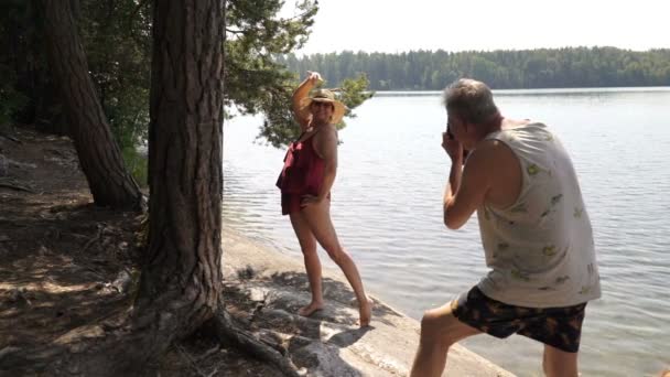 Elderly man taking picture of attractive senior woman with vintage camera on the beach. - Footage, Video