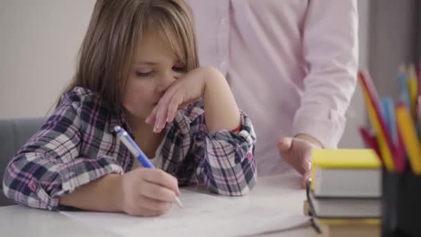 Portrait of upset Caucasian schoolgirl throwing pen on the table and reclining on chair. Unrecognizable mother scolding daughter for problems in education. Studying, lifestyle, homework. - Footage, Video