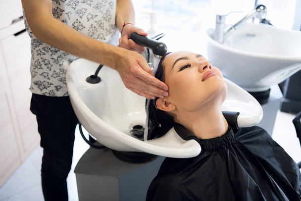 Schönheits- und Personenkonzept - glückliche junge Frau mit Friseurwaschkopf im Friseursalon - Foto, Bild