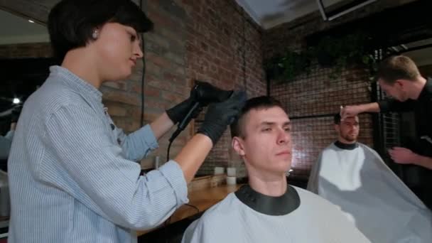Mans hair cutting by barbers scissors and comb with barbershop logo behind in slow motion. Mans hands making male haircut in salon - Footage, Video