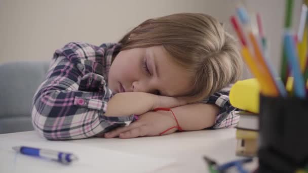 Close-up portrait of tired Caucasian schoolgirl sleeping on the table. Exhausted child getting asleep while doing homework. Education, overload. - Кадры, видео