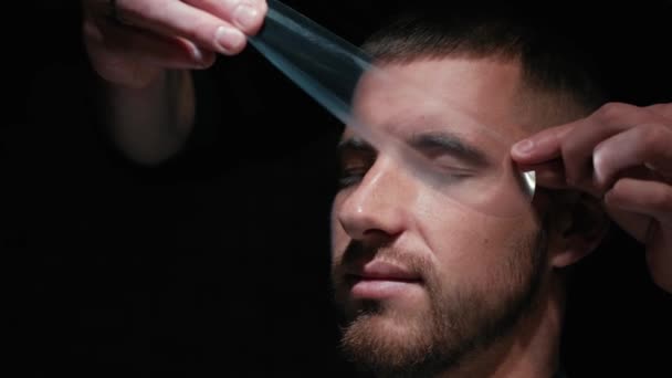 Mans hair cutting by barbers scissors and comb with barbershop logo behind in slow motion. Mans hands making male haircut in salon - Felvétel, videó