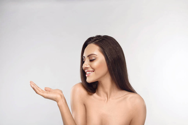 Beauty Face. Beautiful Woman surprise showing product. Laughing brunette model girl with long hair on grey background. Presenting your product. Expressive facial expressions - Foto, imagen
