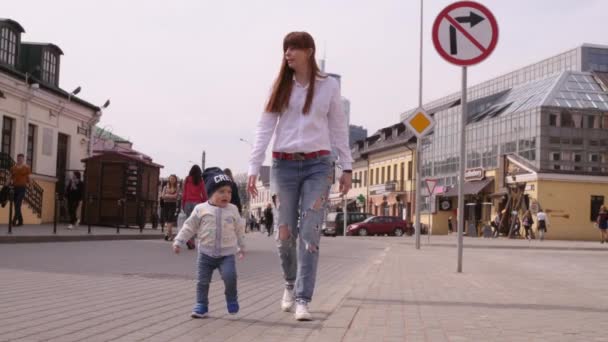 Young beautiful womanand her little baby son are walking on the pedestrian street in the historic center of the city on sunny summer day in slow motion medium shot 4K video. - Filmmaterial, Video