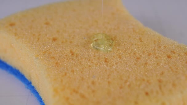 Transparent dishwashing gel is poured onto a yellow porous sponge with a blue base close-up. Macro video - Video