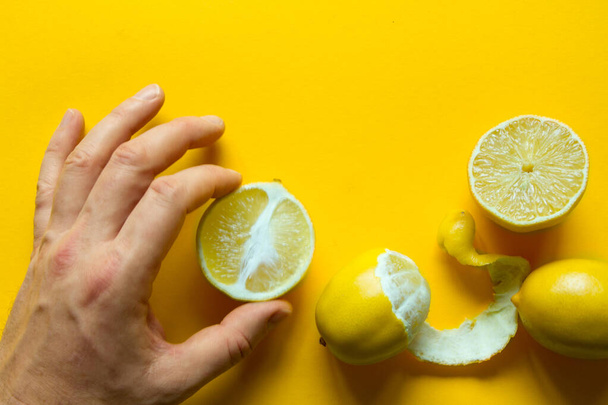 Top view of male hands holding whole and sliced ripe lemons on a yellow surface, concept of health and vitamins - 写真・画像