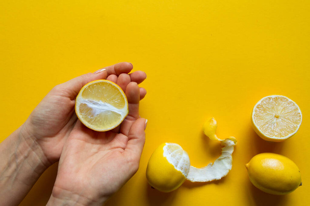 Κάτοψη των γυναικείων χεριών που κρατούν ολόκληρα και κομμένα σε φέτες ώριμα λεμόνια σε κίτρινη επιφάνεια, έννοια της υγείας και των βιταμινών - Φωτογραφία, εικόνα