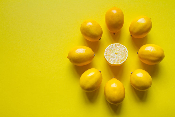 Top view whole and sliced ripe lemons laid out in the shape of a dial on a yellow surface, concept of health and vitamins - Fotoğraf, Görsel