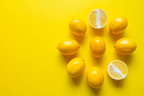 Top view whole and sliced ripe lemons laid out in the shape of a dial on a yellow surface, concept of health and vitamins - Photo, Image