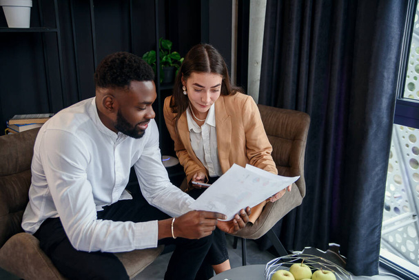 Business couple of african american man and european woman which sitting in specially designated room and using paper documents and tablet pc, conversing about their business project and their - Photo, Image
