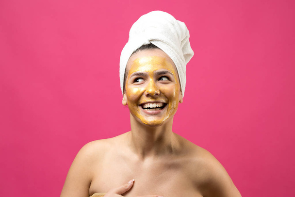 Πορτραίτο ομορφιάς γυναίκας με λευκή πετσέτα στο κεφάλι με χρυσή θρεπτική μάσκα στο πρόσωπο. Καθαρισμός δέρματος eco οργανικό καλλυντικό spa χαλαρώστε έννοια. - Φωτογραφία, εικόνα