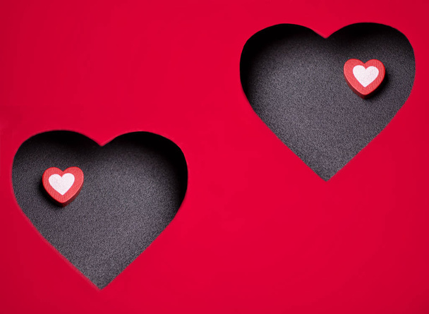 Dois pequenos corações de madeira em uma superfície preta está dentro de um grande coração esculpido em papelão vermelho
. - Foto, Imagem