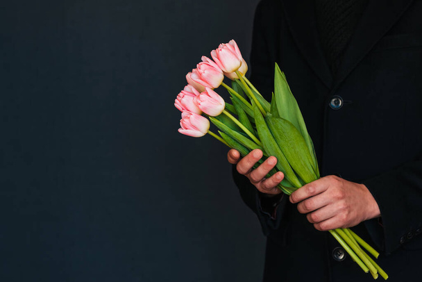 букет розовых тюльпанов в руках мужчины в черном пальто
 - Фото, изображение
