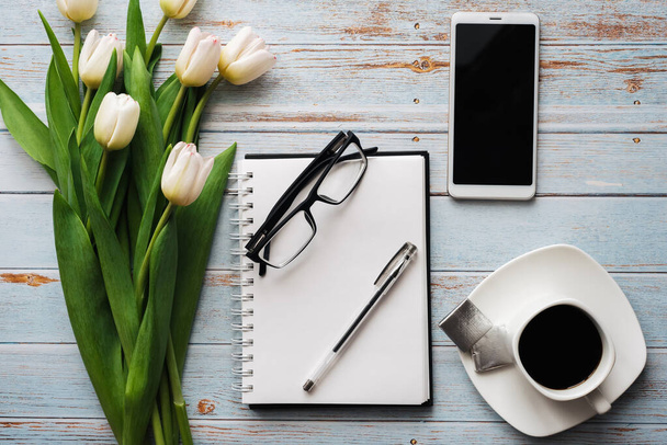Wit boeket tulpen op houten achtergrond met koffiekopje, smartphone en lege notebook - Foto, afbeelding