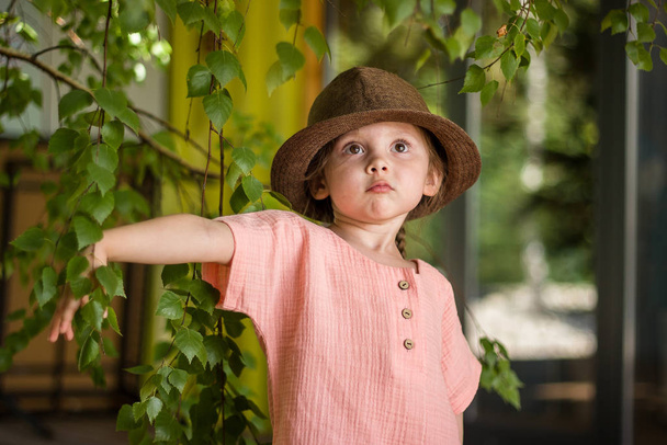 Портрет щасливої милої маленької дівчинки в сільському стилі коричневий капелюх і одяг з мусліну на зеленому дерев'яному фоні в літній день
. - Фото, зображення