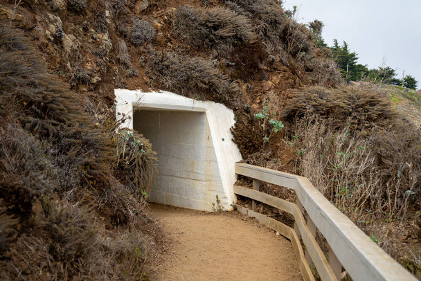 Dirt footpath leading into white tunnel in coastal cliff line - Photo, Image