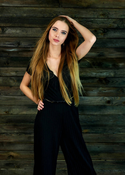 The concept of glamor, style. Model Stands in different poses in front of the camera. Vertical portrait of a pretty blonde girl with long hair and great makeup on a wooden background. - Foto, imagen