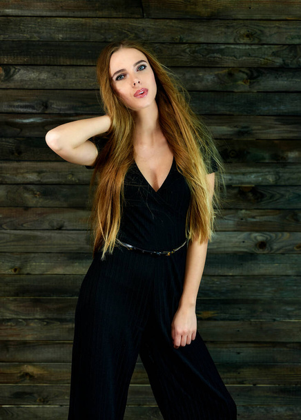The concept of glamor, style. Model Stands in different poses in front of the camera. Vertical portrait of a pretty blonde girl with long hair and great makeup on a wooden background. - Foto, afbeelding