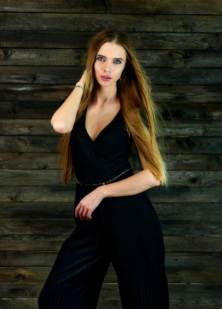 The concept of glamor, style. Model Stands in different poses in front of the camera. Vertical portrait of a pretty blonde girl with long hair and great makeup on a wooden background. - Zdjęcie, obraz