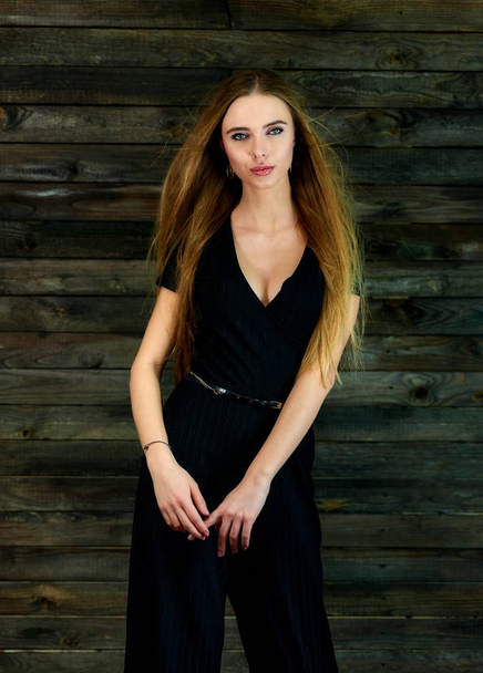 The concept of glamor, style. Model Stands in different poses in front of the camera. Vertical portrait of a pretty blonde girl with long hair and great makeup on a wooden background. - Foto, imagen