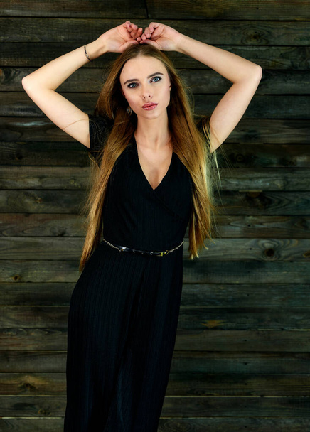 The concept of glamor, style. Model Stands in different poses in front of the camera. Vertical portrait of a pretty blonde girl with long hair and great makeup on a wooden background. - Foto, immagini