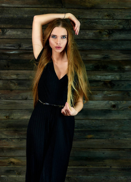 The concept of glamor, style. Model Stands in different poses in front of the camera. Vertical portrait of a pretty blonde girl with long hair and great makeup on a wooden background. - Fotó, kép