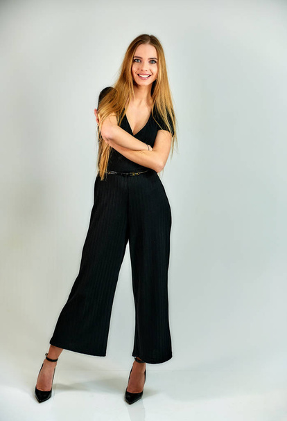 The model stands in different poses in front of the camera. The concept of fashion and style. Full-length portrait of a pretty blonde girl with long hair and excellent make-up on a white background. - Foto, Bild
