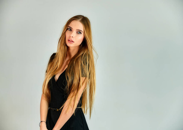 The concept of fashion and style. Portrait of a pretty blonde girl with long hair and great makeup on a white background. The model stands in different poses in front of the camera. - Foto, Imagen