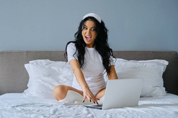 Beautiful brunette woman sitting in bed using laptop computer - Foto, Bild