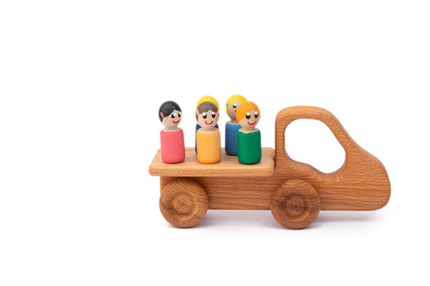 Houten speelgoedauto aangedreven door veelkleurige mannen op een witte geïsoleerde achtergrond. Concept bouwplaats - Foto, afbeelding